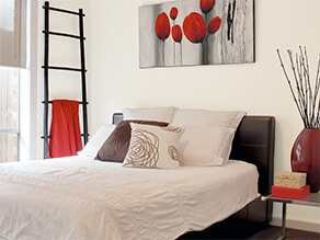 Neutral bedroom with pops of red colour in artwork, towels and decorations, ladder plant and pillows